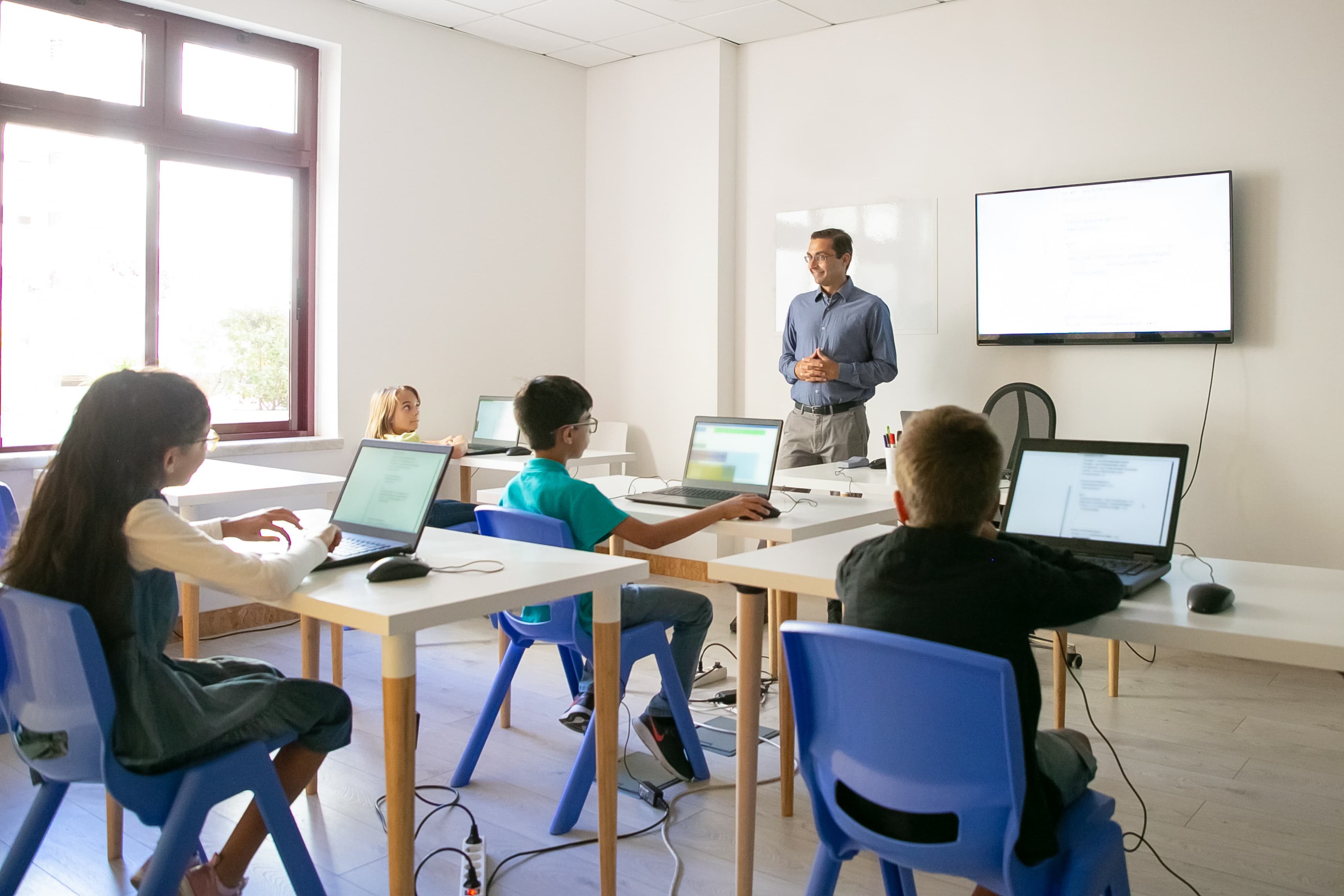 Students in a modern classroom with laptops and a teacher at the front